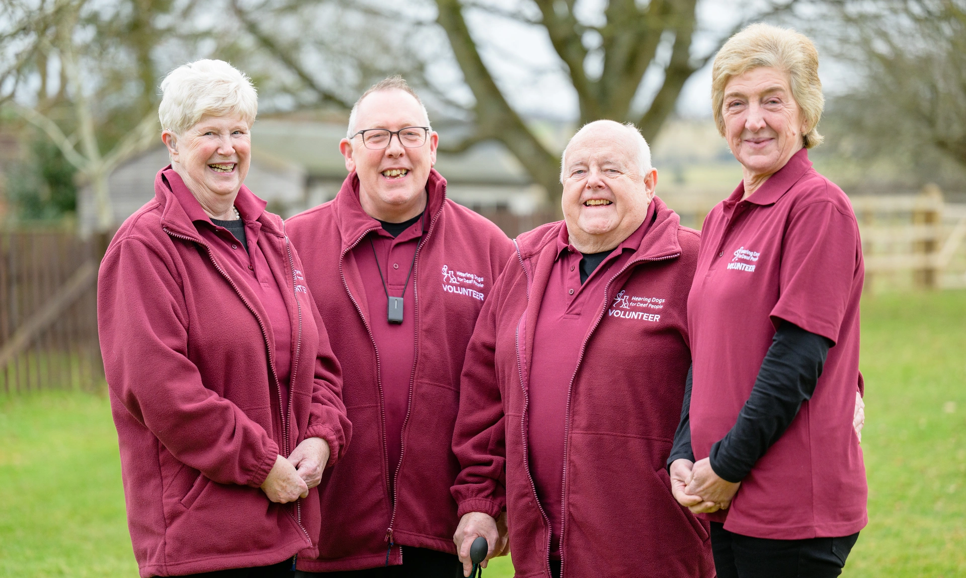 A group of happy looking hearing link services volunteers, stood together outside smiling at the camera