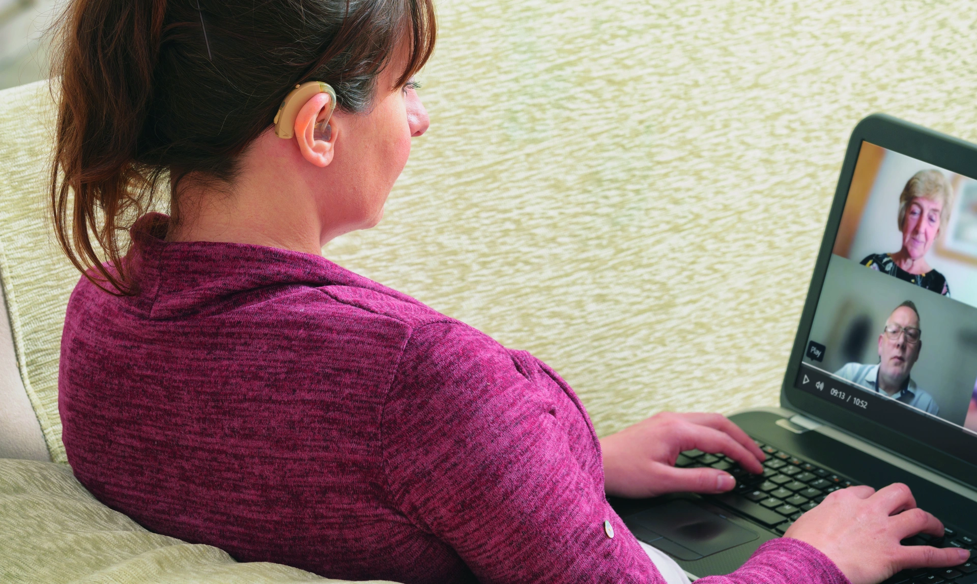 A woman is sat on a sofa with a laptop on her lap, there is a group chat on the screen