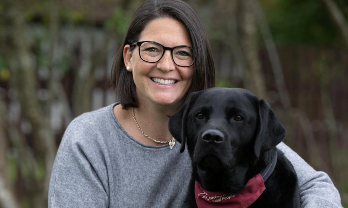 A woman sat with arms round a black labrador
