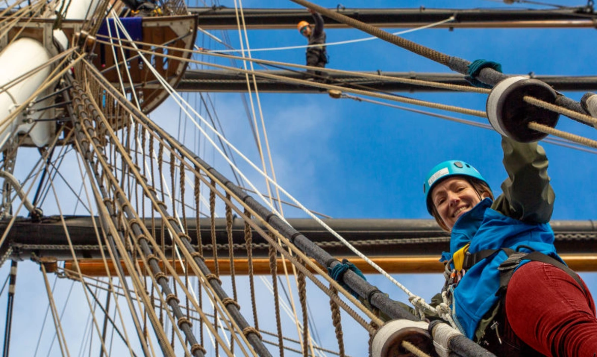 A woman climbing the rigging of a sailing ship, photographed from below