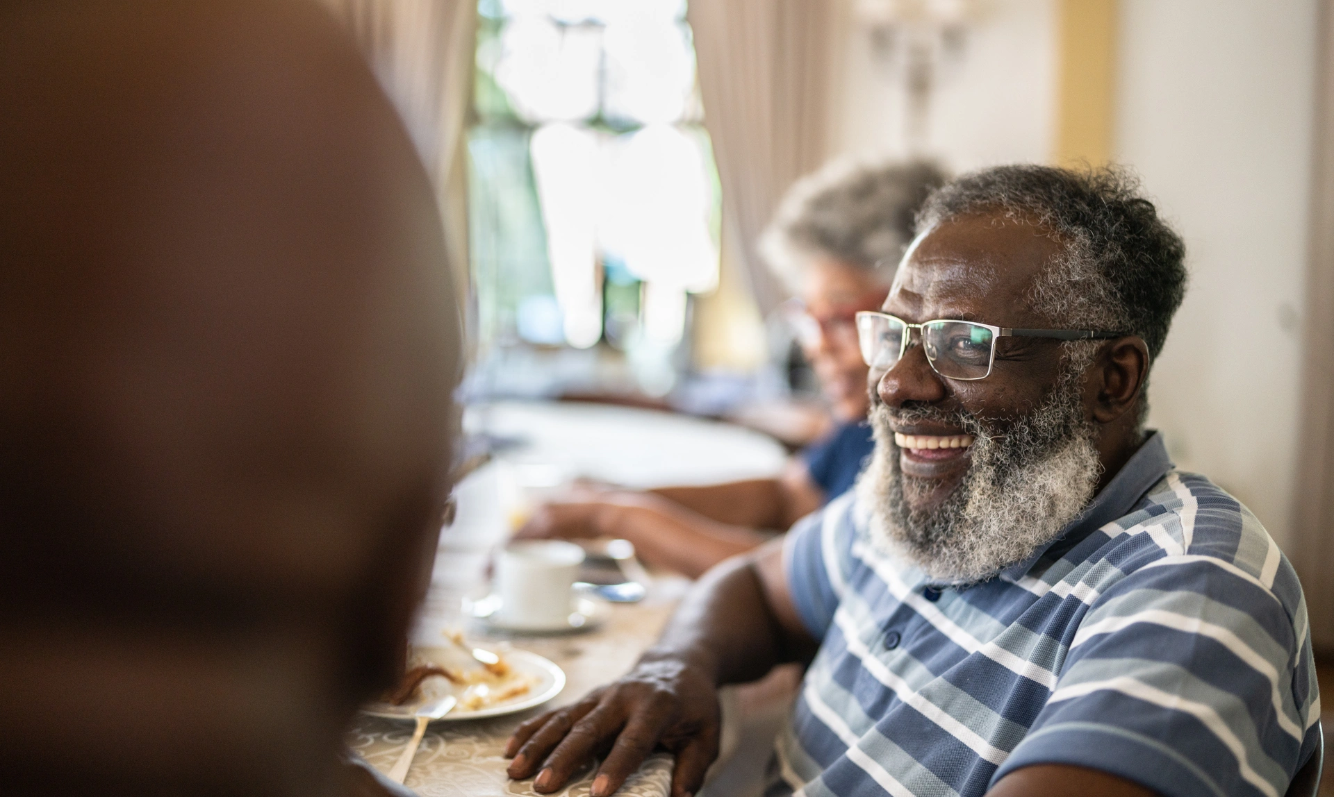 A group of people sitting at a table. The photo is taken with a blurred image of the back of a man's head on the left side.