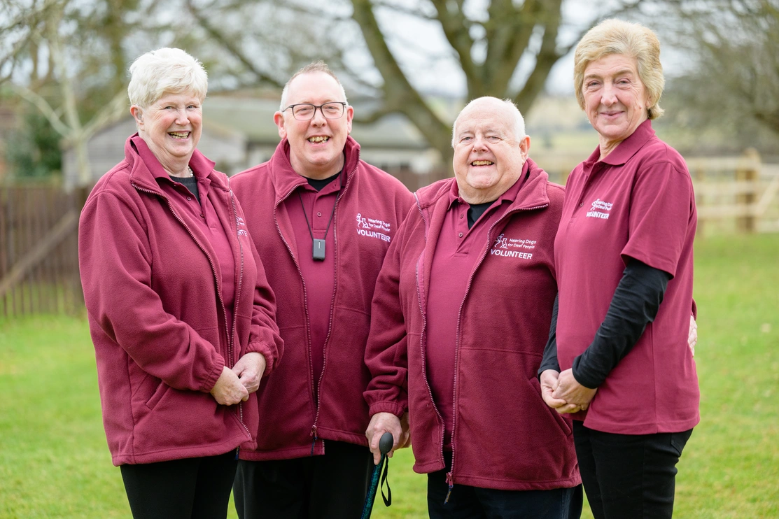 A group of happy looking hearing link services volunteers, stood together outside smiling at the camera