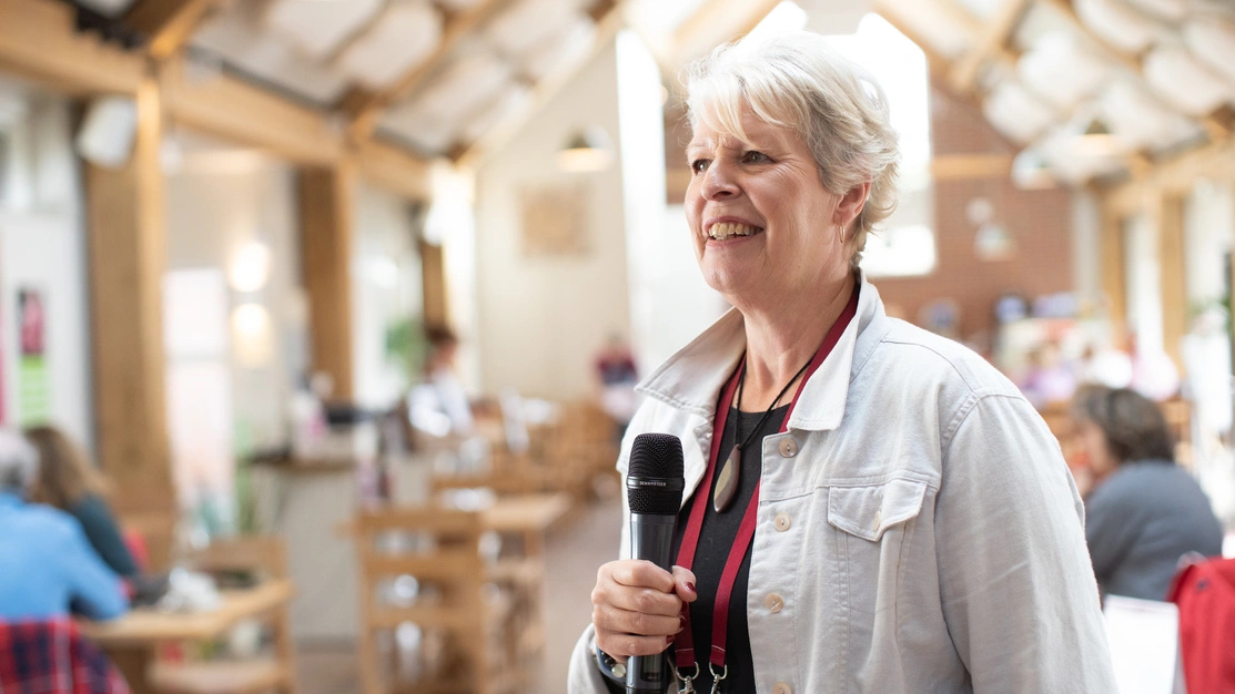 A woman talking and looking happy holding a microphone with people sat behind her