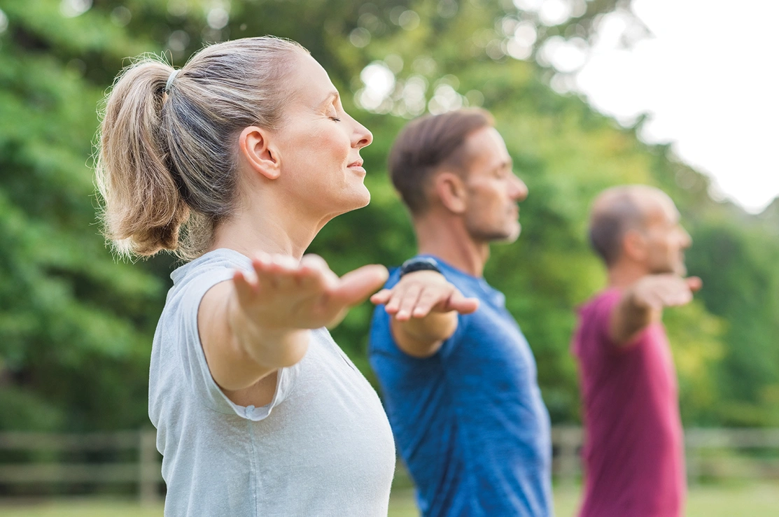 Mid shot of three people stood with their eyes closed and their arms out to their sides