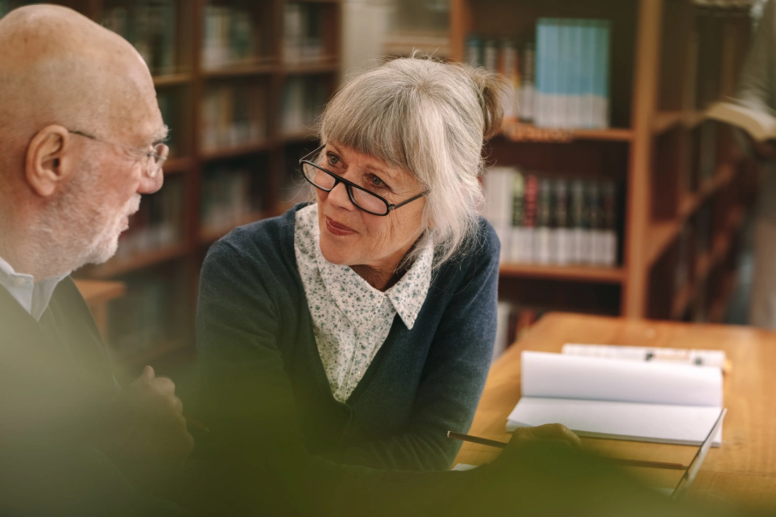 Mid shot of a man and a woman sat at a table having a conversation, the woman is leaning towards the man and focussing on his mouth