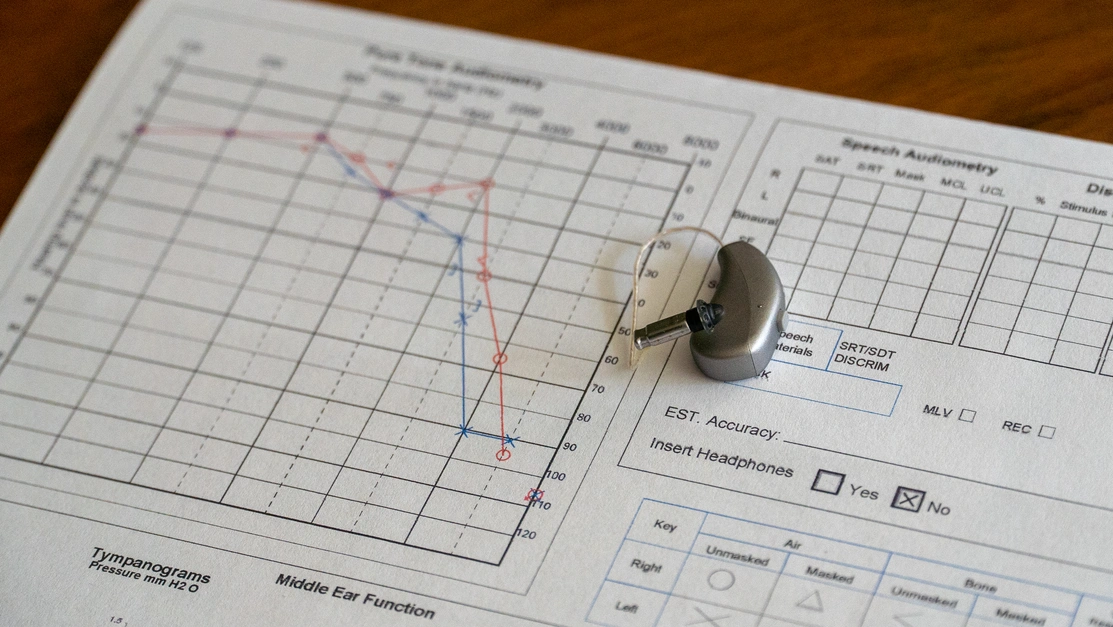A printed audiogram on a wooden table with a small hearing device on top of it