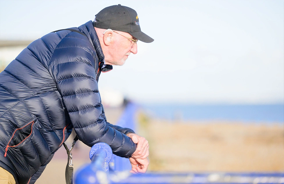  Mid shot of an older man leaning on some railings and looking into the distance with a seafront in the background