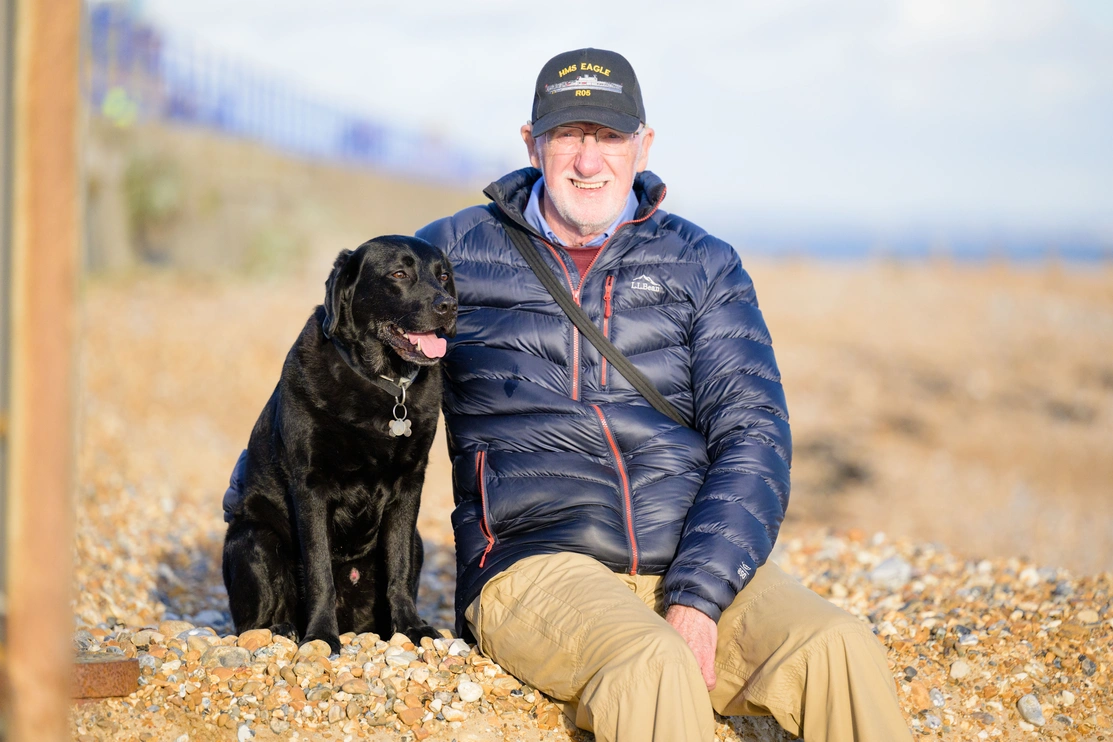 Deryck and hearing dog Elroy sat on a pebble beach