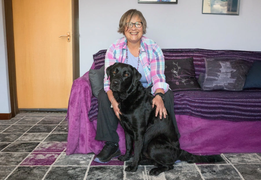 A woman sitting on a sofa. A black labrador dog is in front of her