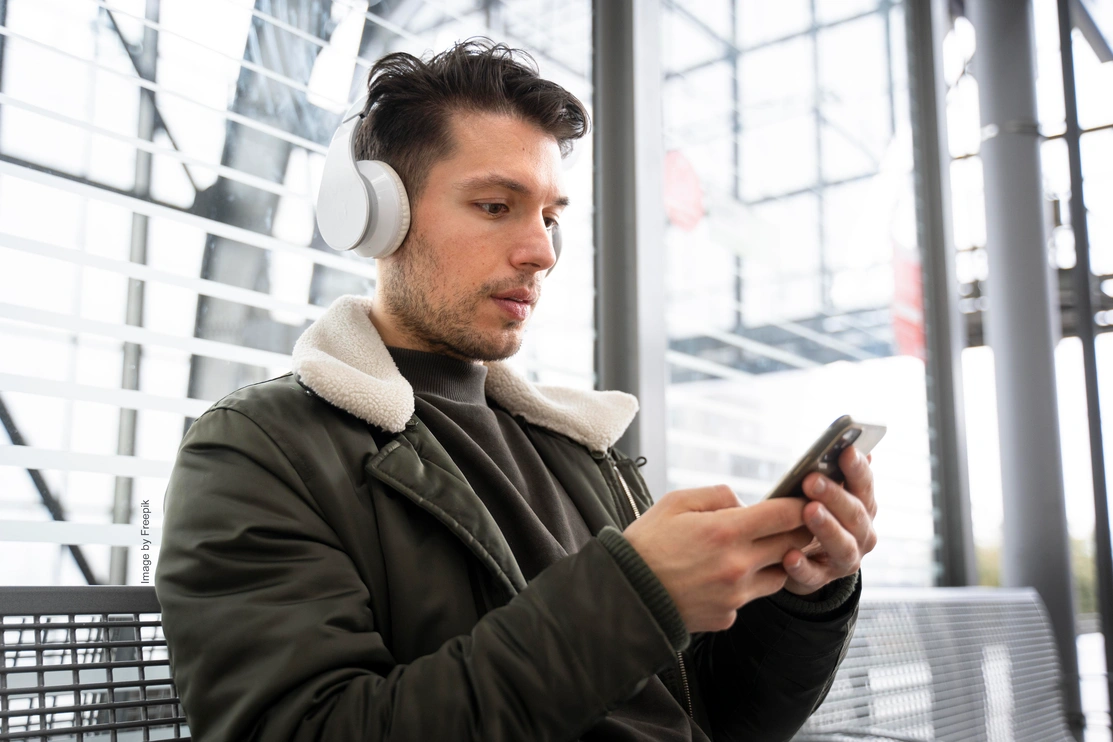 Man holding a mobile phone with headphones on concentrating on the phone screen