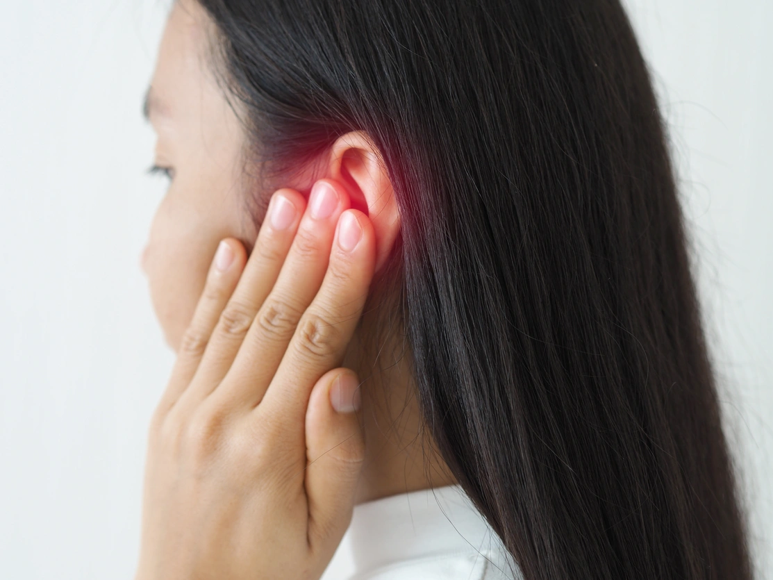 Close up, side view of a woman with her hand to her ear and a red glow around her ear