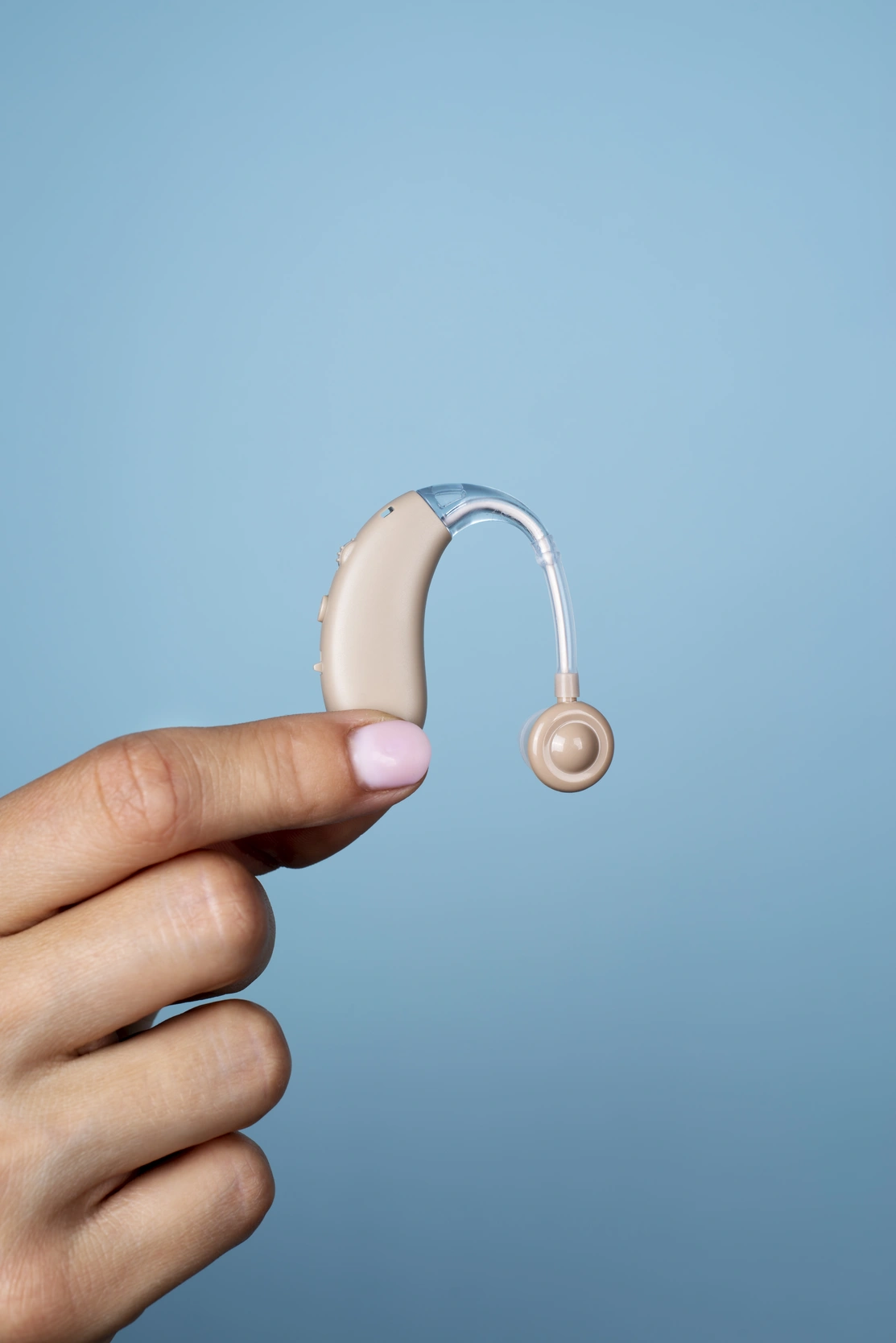 A side view of a hand with a nail painted, holding a hearing aid