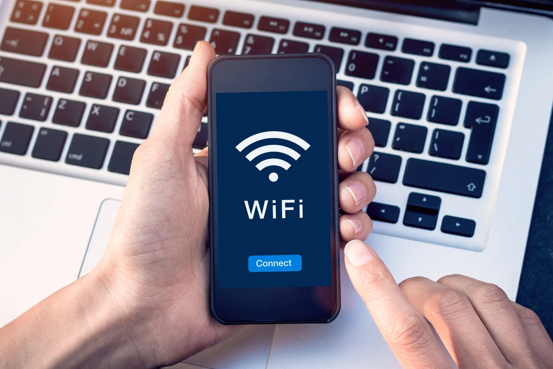 A hand holding a phone over the top of a laptop keyboard, with the wifi symbol and a 'Connect' button on the phone screen
