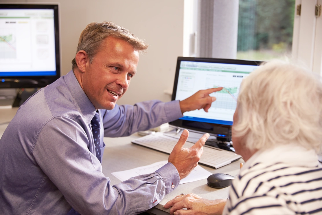 Audiologist sat looking at a patient while he smiles and points to a screen