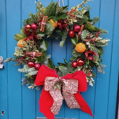 A christmas wreath with a large red bow, hanging on a blue wooden door