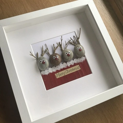 A box frame with pebbles decorated as Christmas reindeer inside