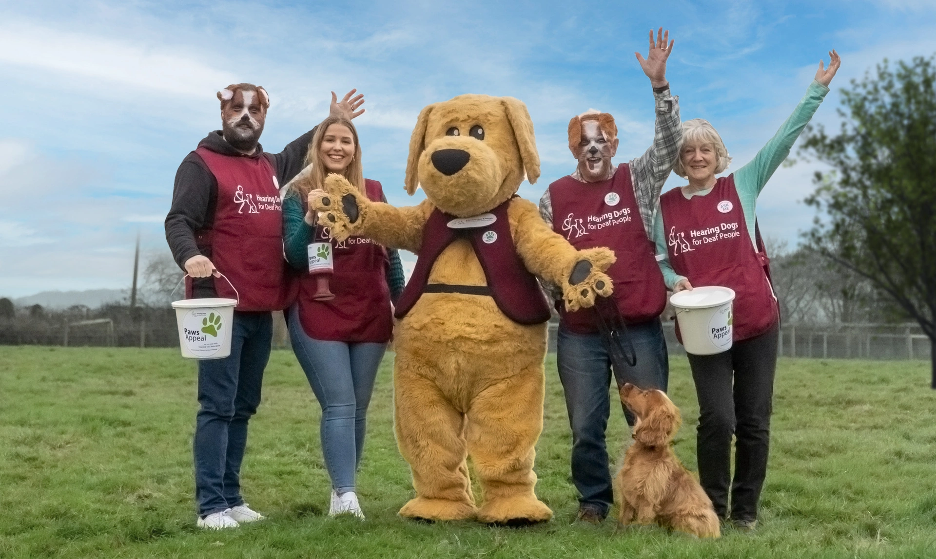 A group of people waving. In the middle is someone dressed in a dog costume