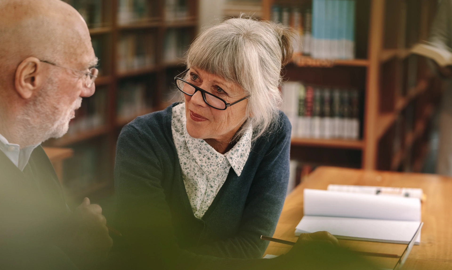 Mid shot of a man and a woman sat at a table having a conversation, the woman is leaning towards the man and focussing on his mouth
