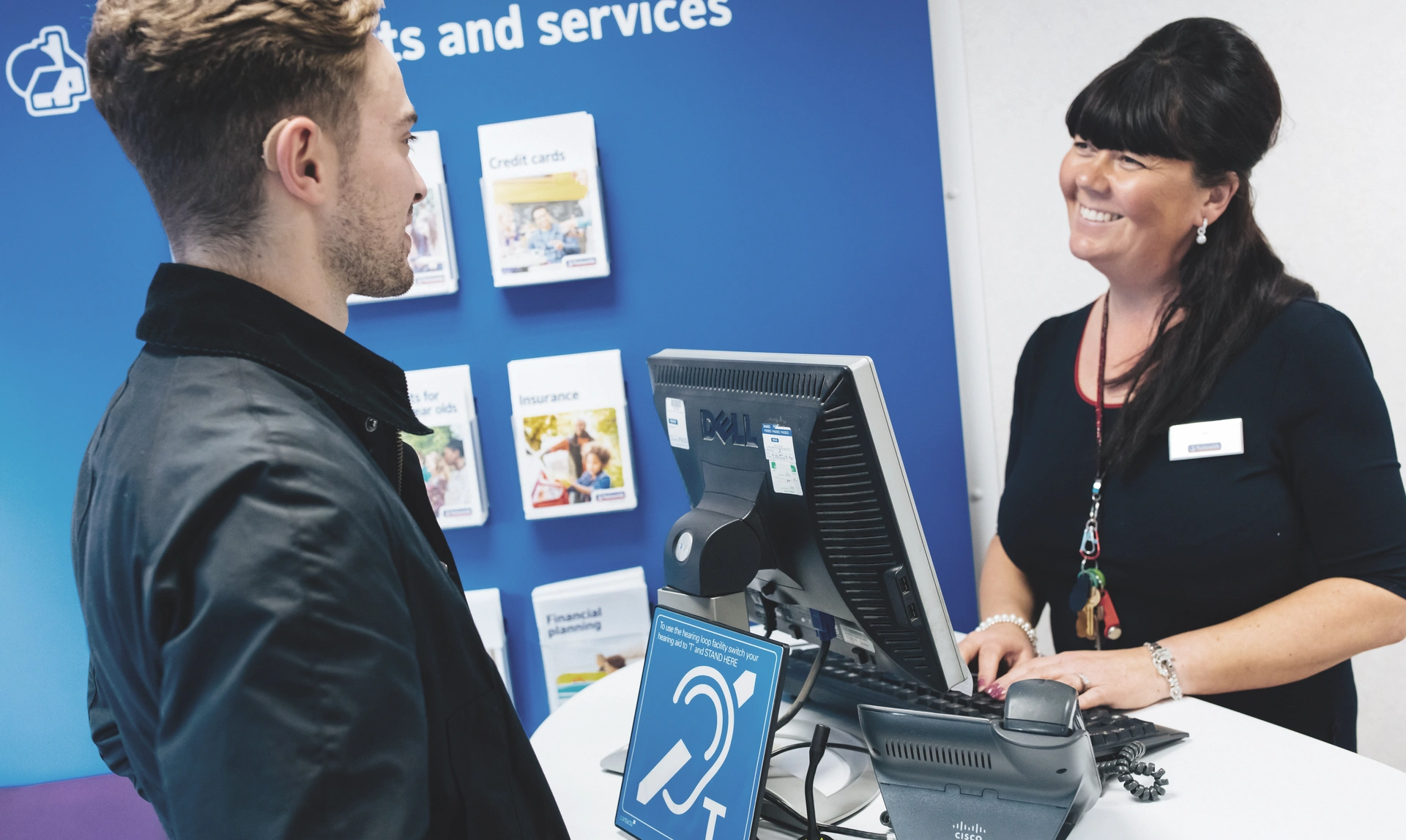 A women serving a man who is wearing a hearing aid at a bank desk