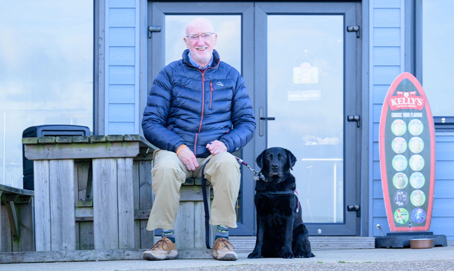 Deryck and hearing dog Elroy sat ouside a blue beach shack