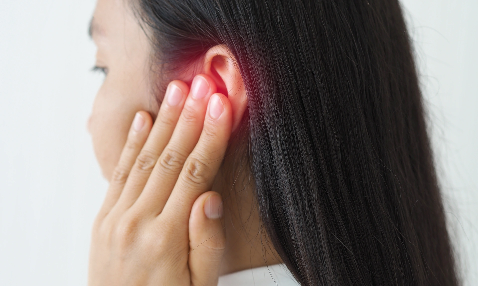 Close up, side view of a woman with her hand to her ear and a red glow around her ear