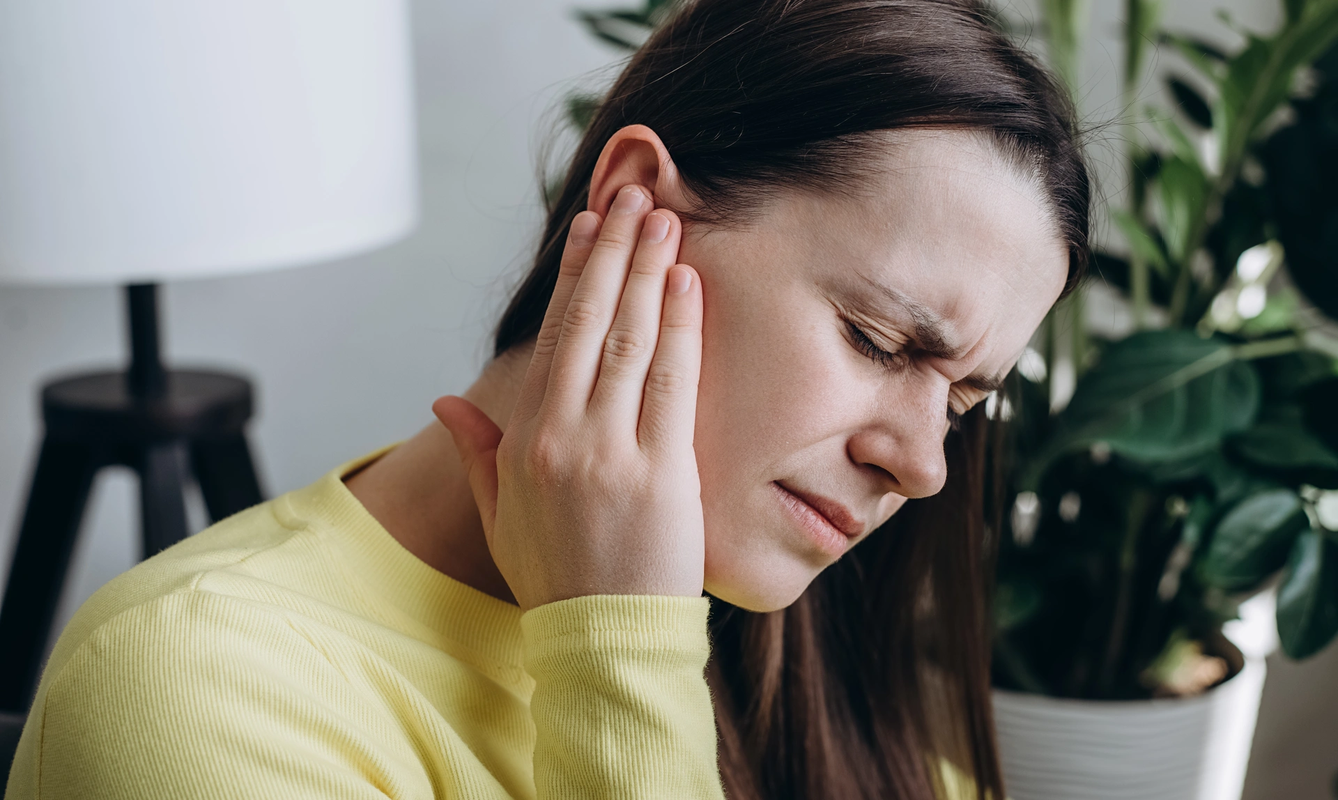 Close up profile of a woman rubbing one of her ears with her eyes closed and a stressful expression