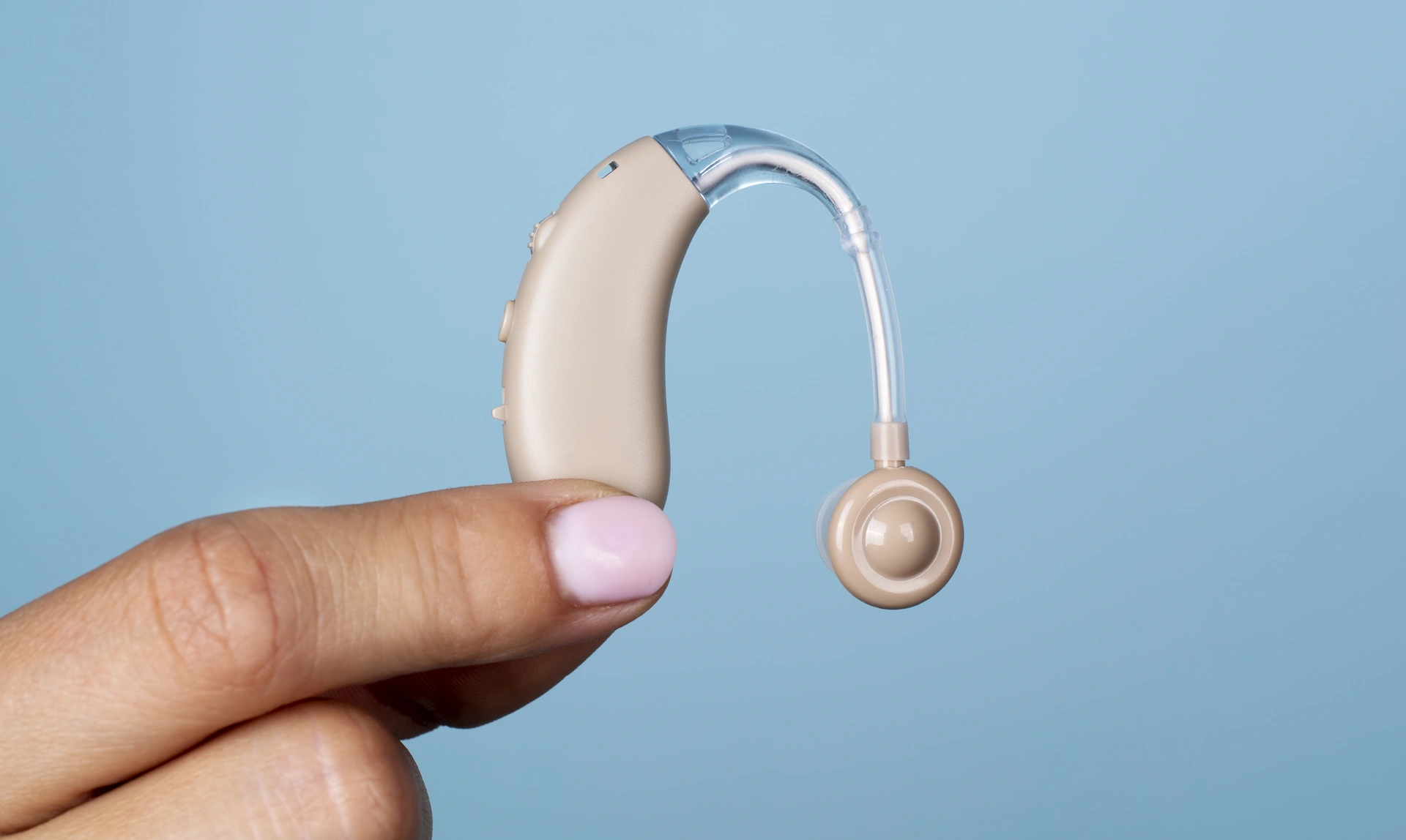 A side view of a hand with a nail painted, holding a hearing aid