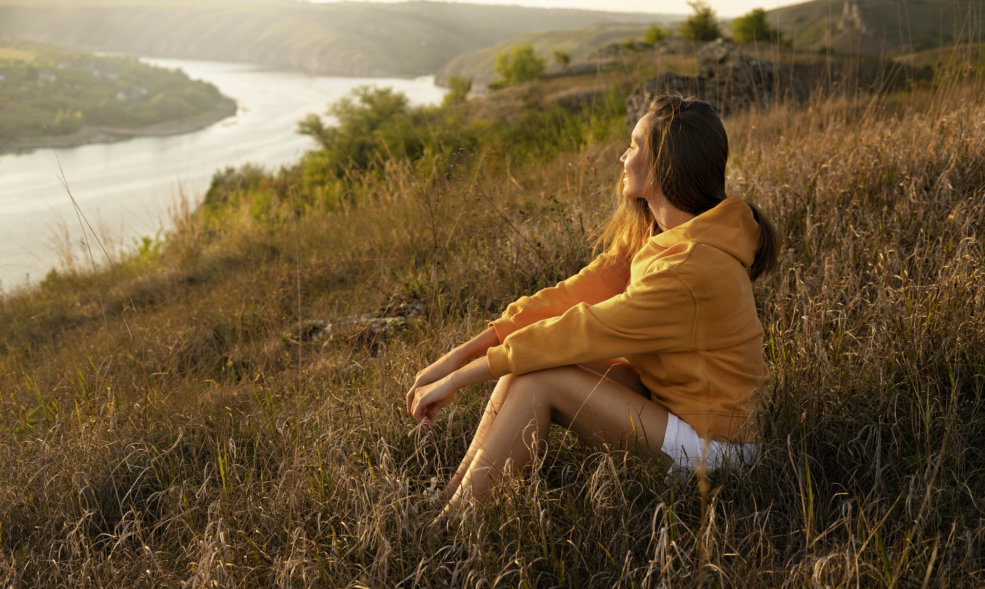Image of a young woman sat on a hillside as the sunsets