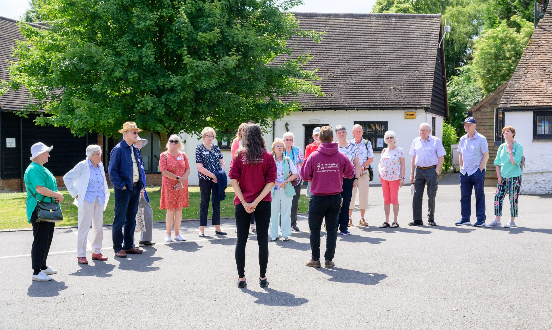  Group of visitors looking at a Hearing Dogs members of staff as they talk outside in the sunshine by some buildings