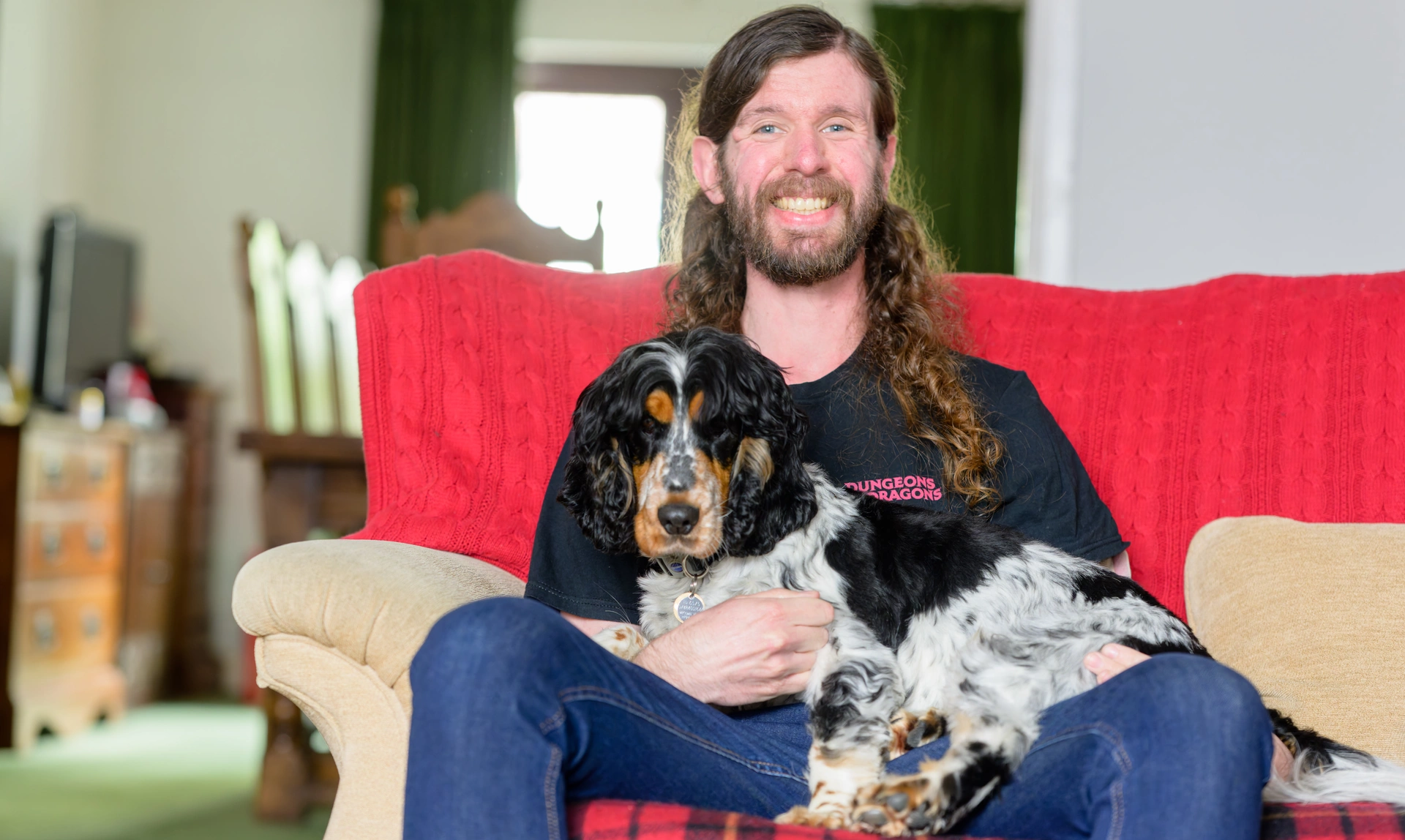 A man sat on a sofa looking happy while his spaniel sits across his lap