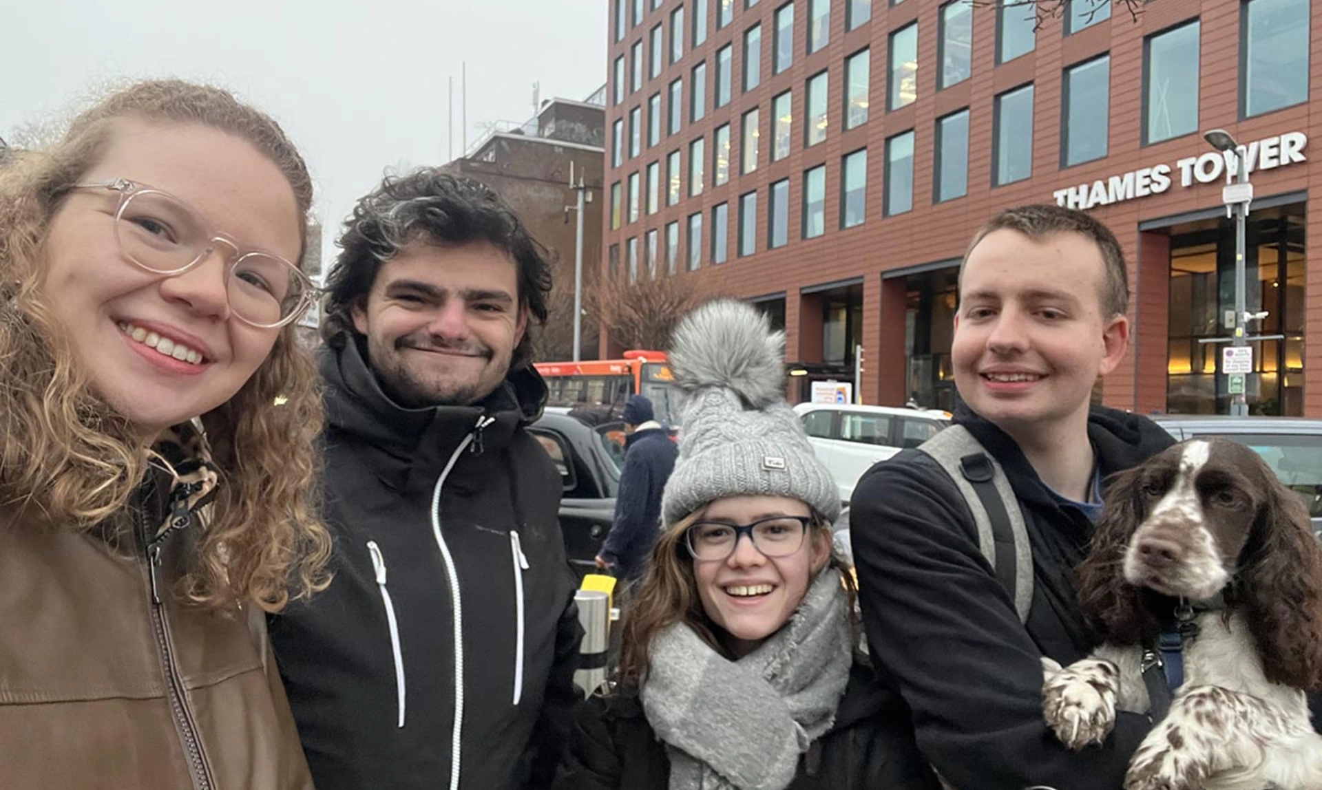 A group of 4 young men and women. On the right, Luke is holding hearing dog Lucy in his arms.