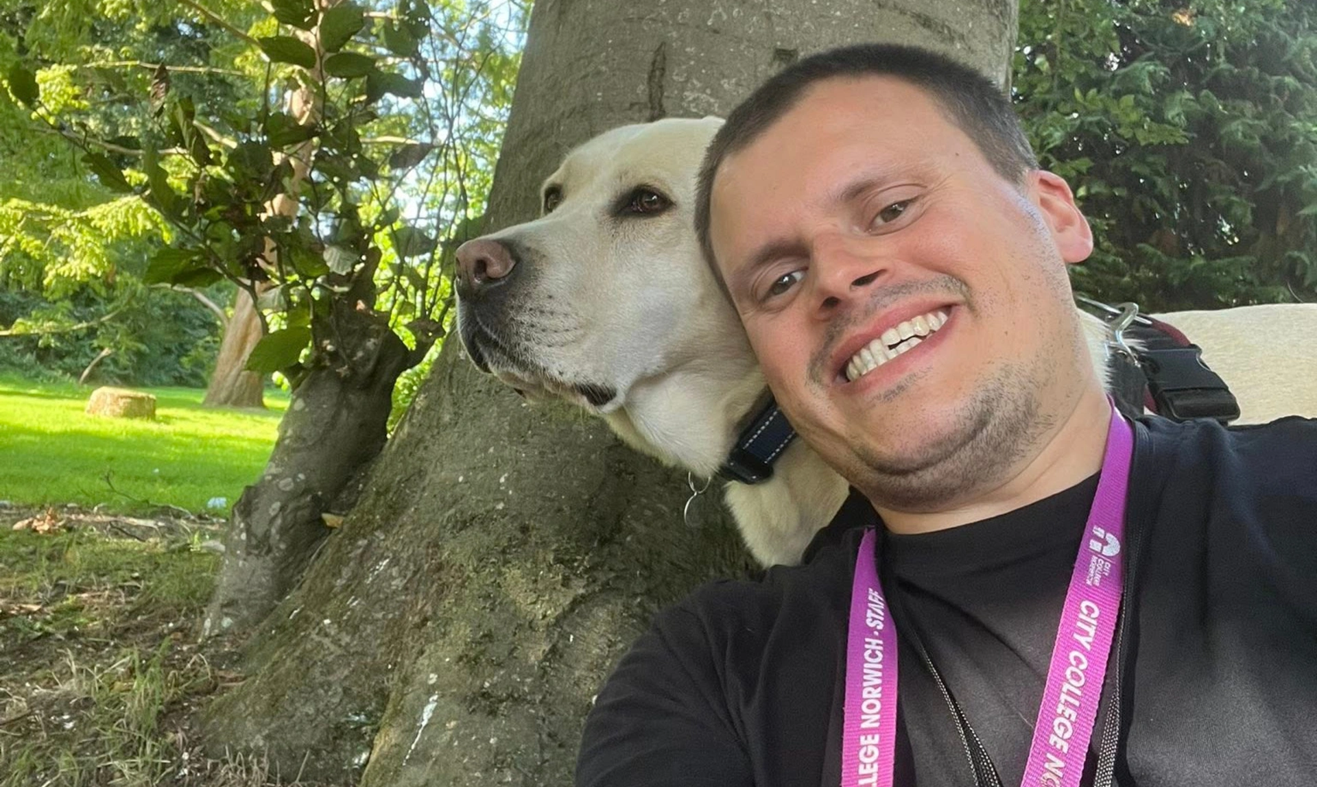 A man and a white labrador in a selfie style photo beside a tree. The main is smiling broadly.