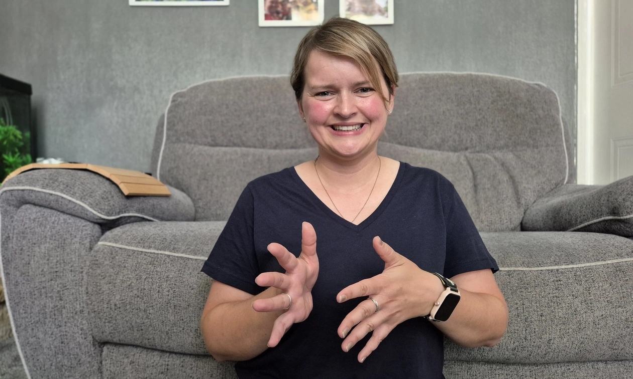 A young woman in a dark blue shirt, her hands in front using sign language gestures
