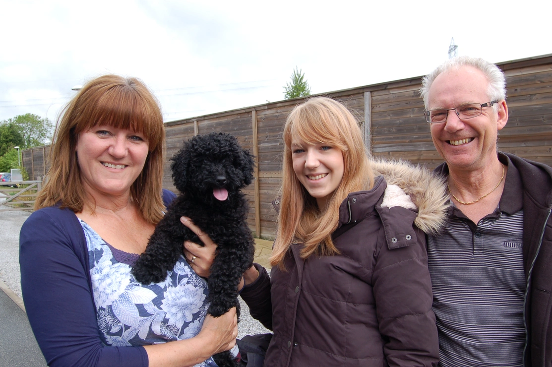 Woman holding black cockapoo with a woman and man standing by her side