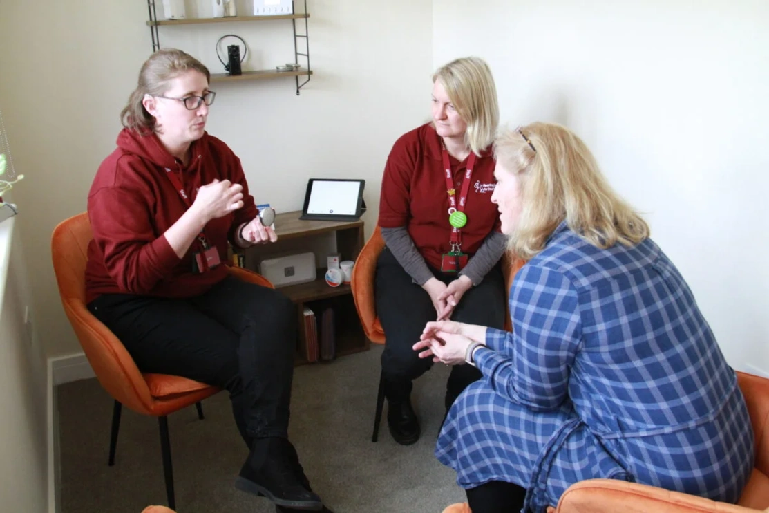 A group of women, one of whom is demonstrating a piece of hearting loss technology