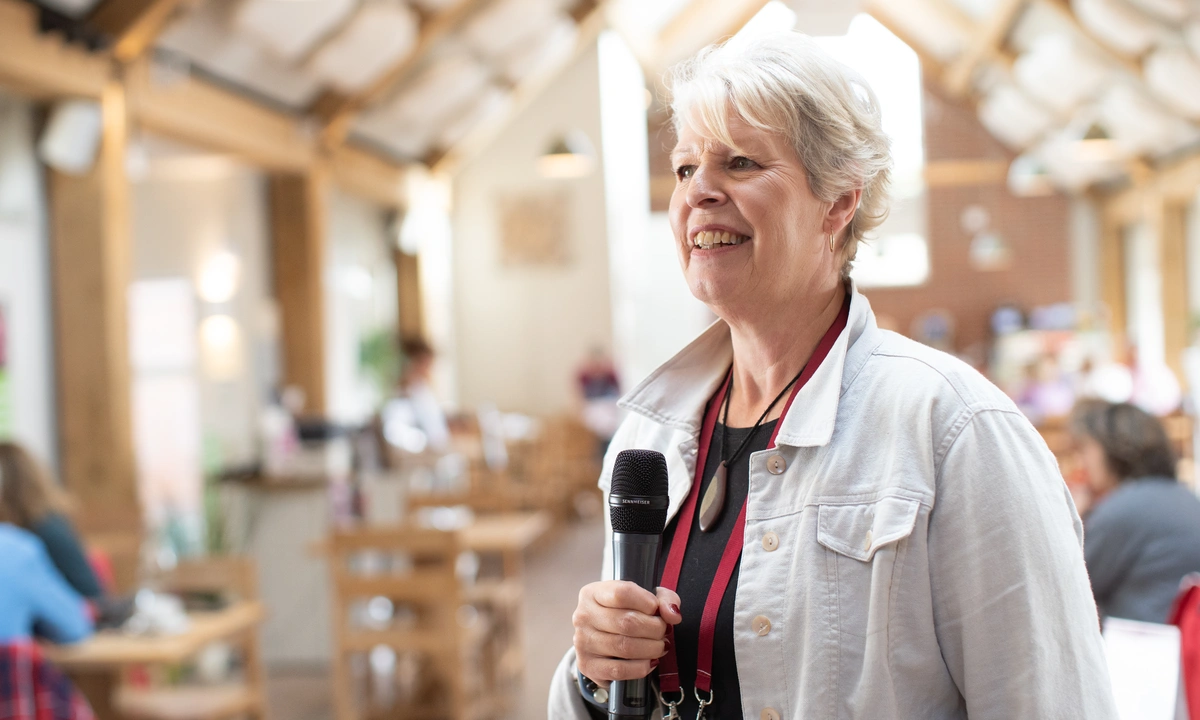 A woman talking and looking happy holding a microphone with people sat behind her
