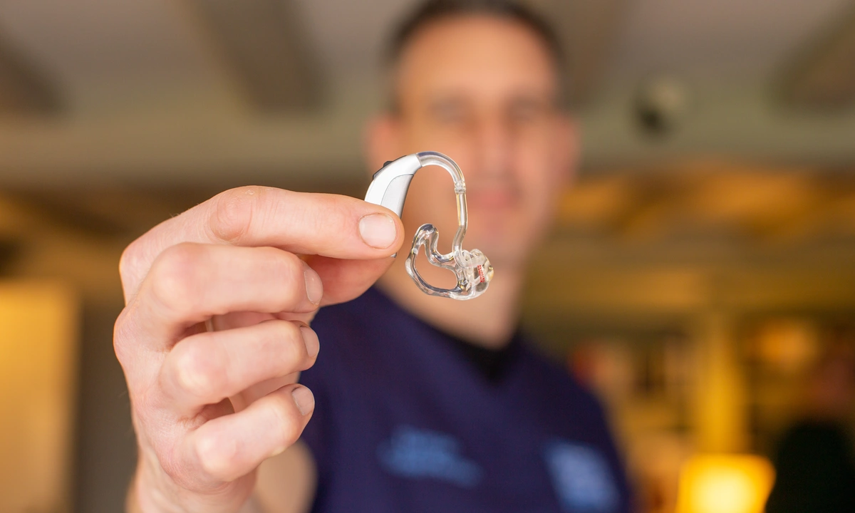 Close up of a hearing aid held by an audiologist, only the hearing aid and audiologist’s hand are in focus the rest of the image is blurry