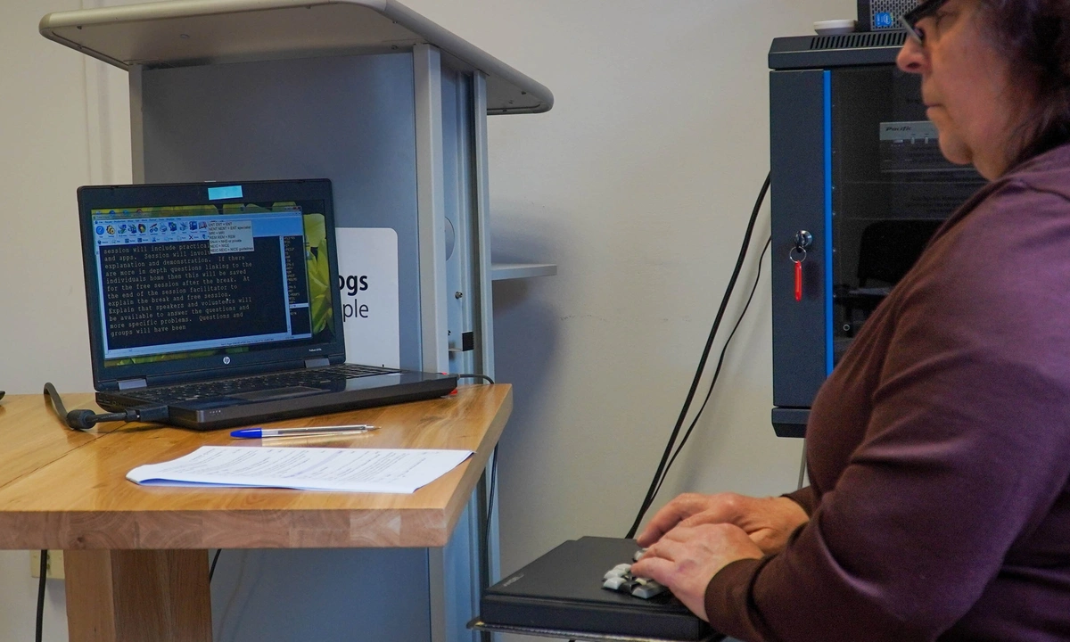 A woman is sat reading a screen which shows speech being transcribed to text