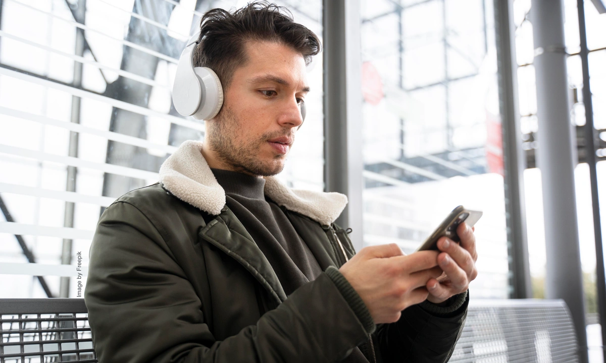 Man holding a mobile phone with headphones on concentrating on the phone screen