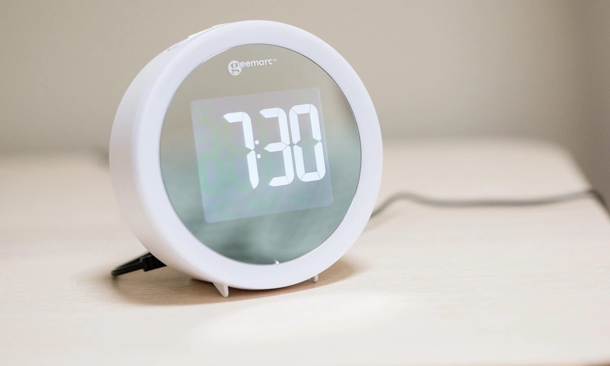 An alarm clock on a table that shows a digital display reading 7:30