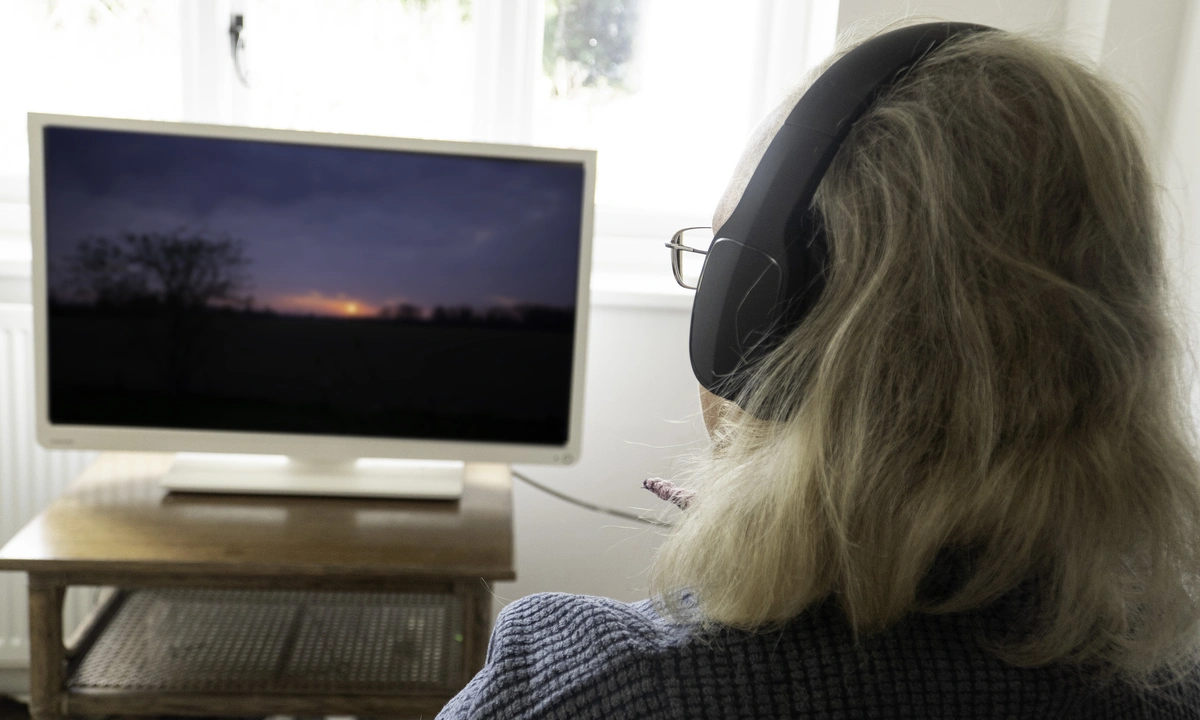 Over the shoulder image of a person sat wearing wireless headphones watching television