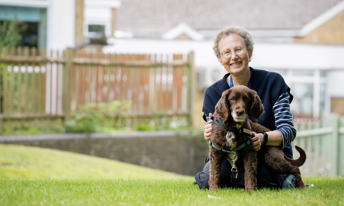 A smiling woman and a brown dog pose for the photo on a grassy area.