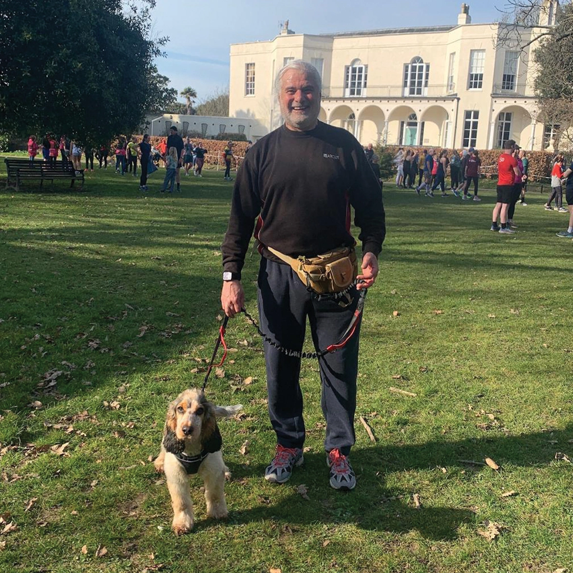 Man standing on grass with sable cocker spaniel next to him on lead