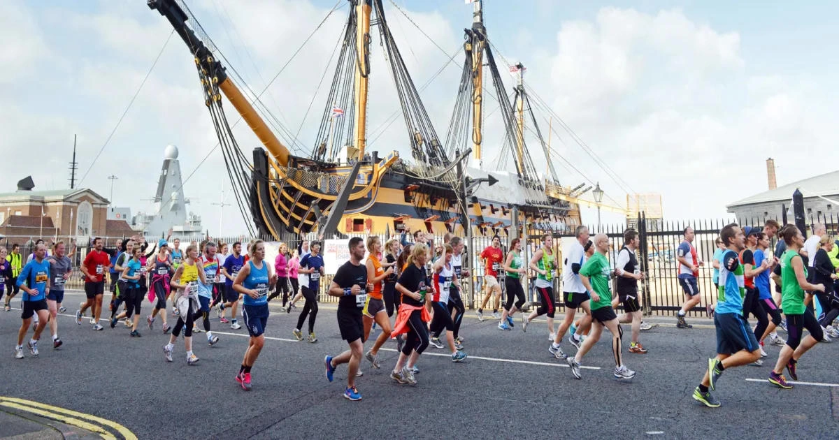 Photo depicting a group of runners as they pass a large sailing ship in the background