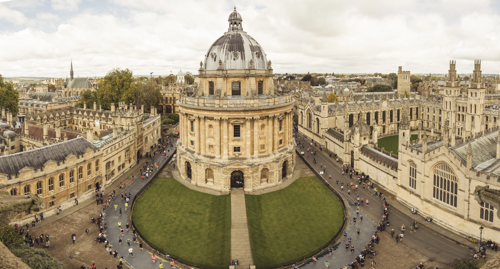 An aerial photo of runners rounding the Radcliffe Camera library building at oxford university. It is a large circular domed building
