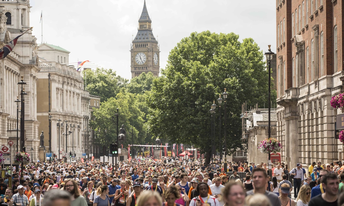 A large crowd of people gathered in London street. Big Ben clocktower can be seen in the background behind some trees.