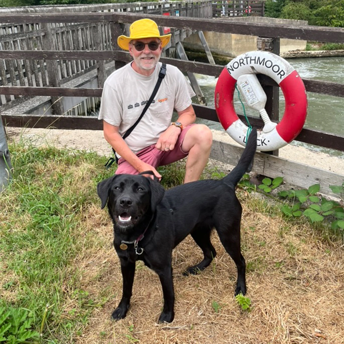 A man wearing a yellow hat and a black Labrador standing next to a Lock