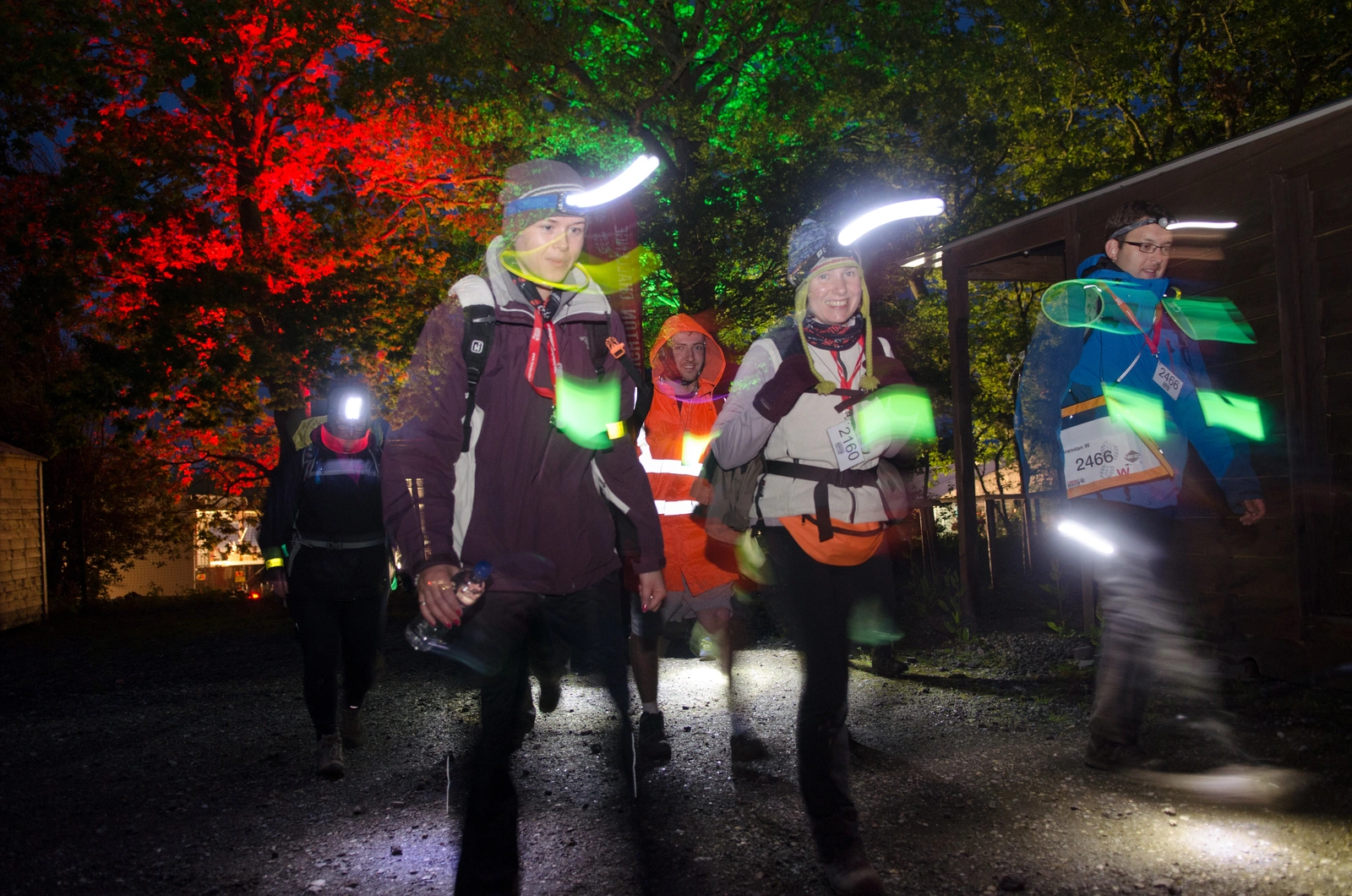 A group of people, wearing warm winter clothing and wearing safety lamps, walking at night. The image is a long exposure with blurred lighting.