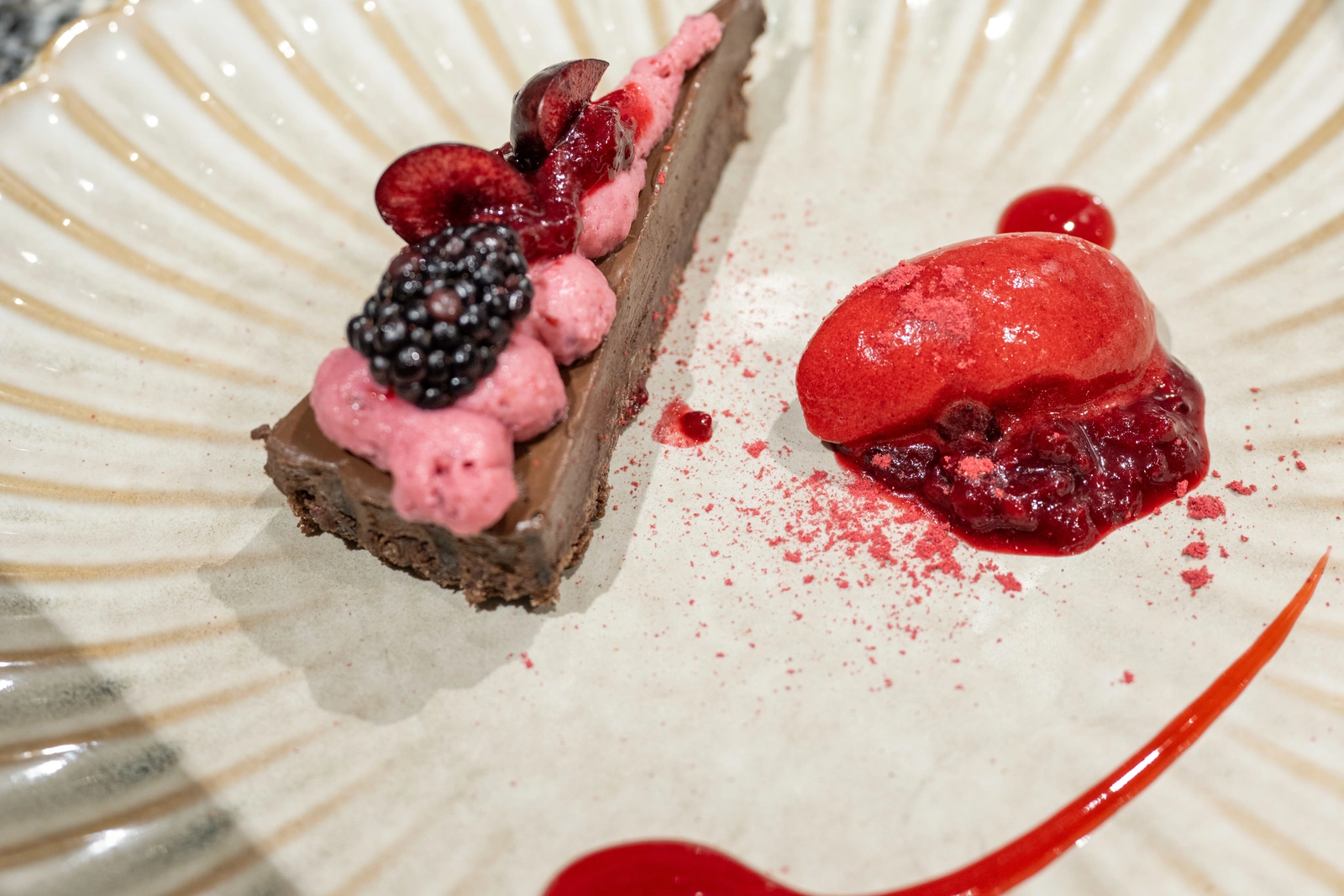 A plated dessert with lots of red berries and triangular chocolate cake slice