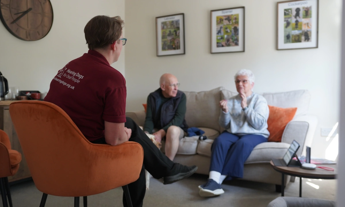 A man and woman in conversation seen from over the shoulder of a woman in hearing dogs staff uniform